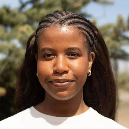 Close-up of a young woman with braided hair, smiling outdoors.