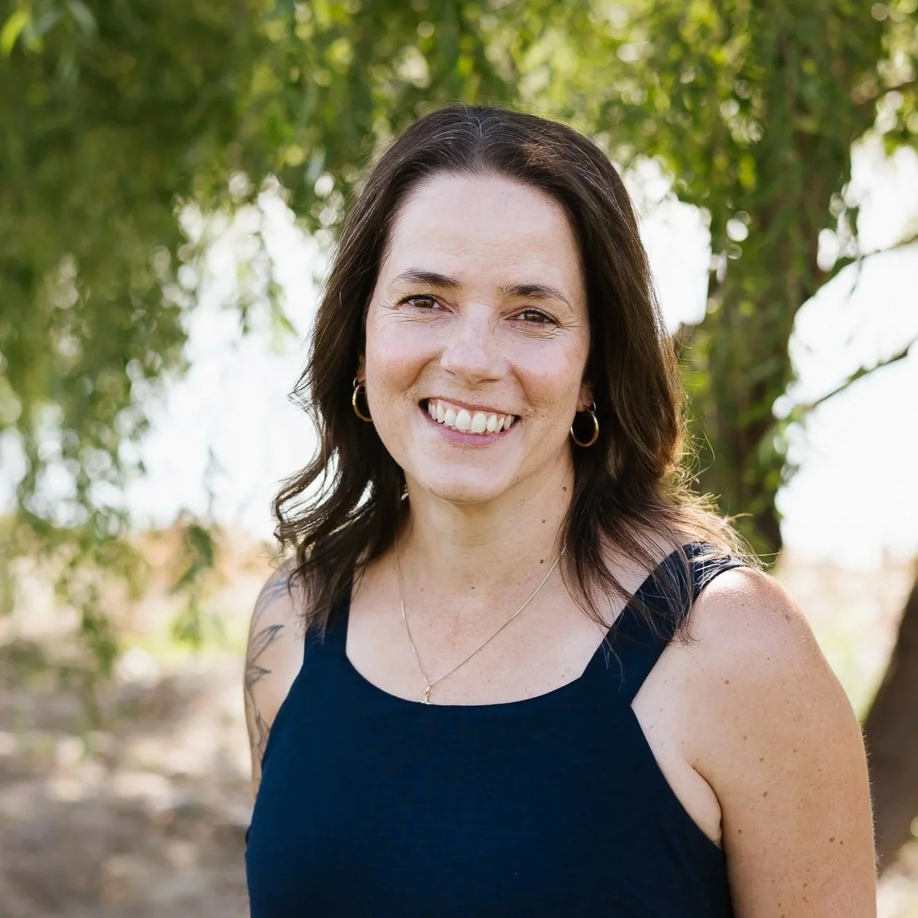 Portrait of a smiling woman with shoulder-length brown hair outdoors, with a blurred green background.
