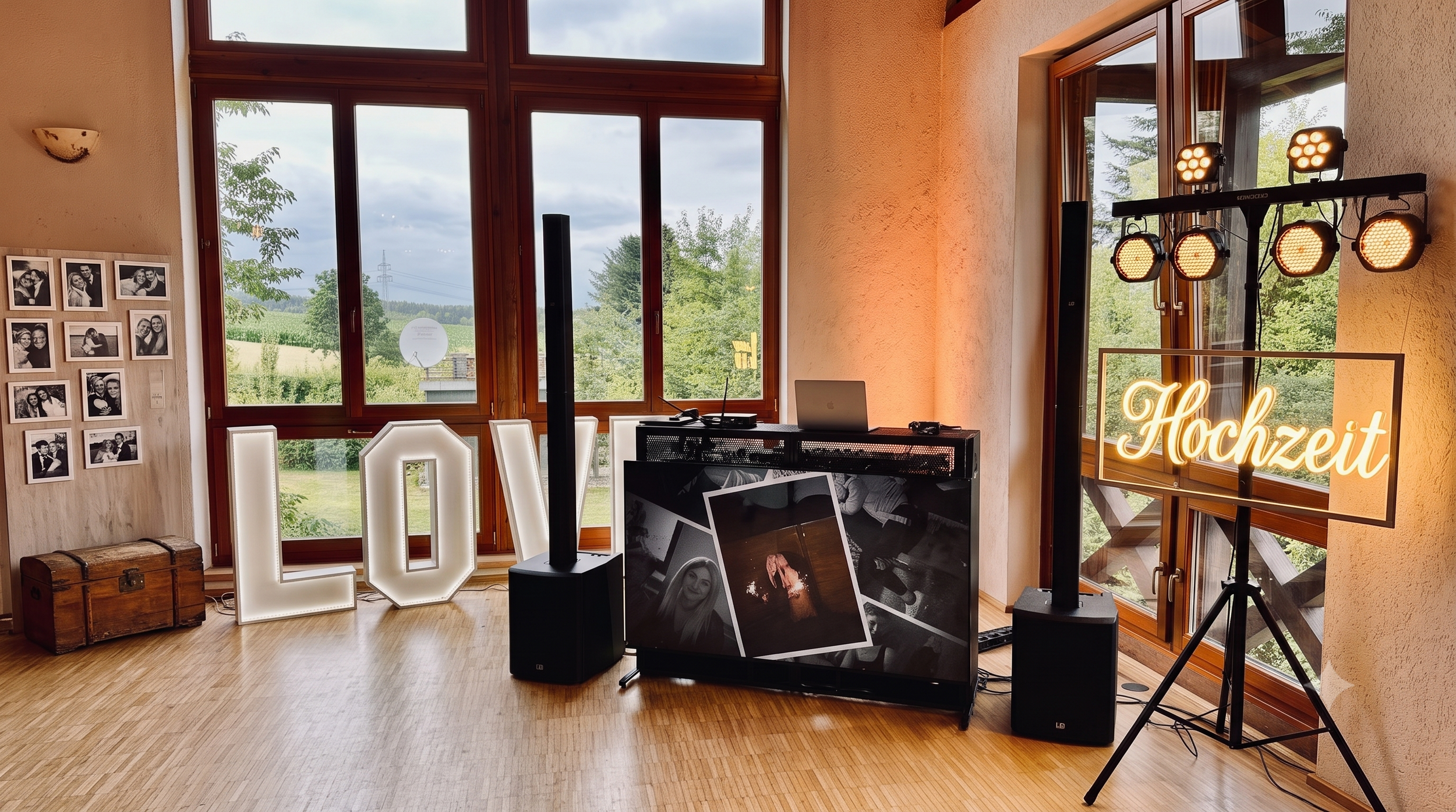 Ein Raum mit großen Fenstern, einer Beleuchtungsanlage für eine Hochzeit, einem Laptop, Wandbildern und einem beleuchteten Schilder mit dem Wort 'Hochzeit'.