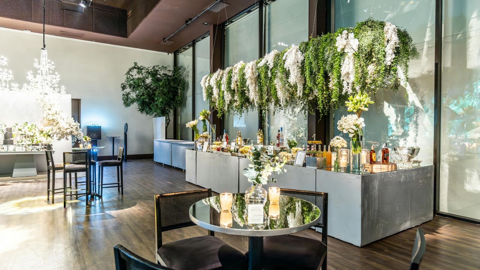 Elegant event space decorated with white and green floral arrangements, candles, and a chandelier.