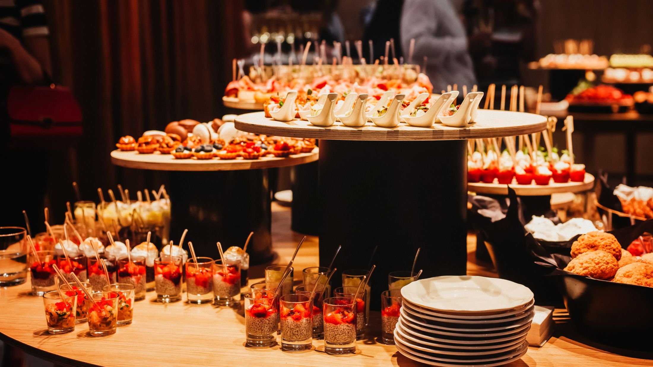 A buffet table filled with assorted desserts, including parfait glasses with berries and cream, small pastries, and other sweet treats, in a warmly lit setting.