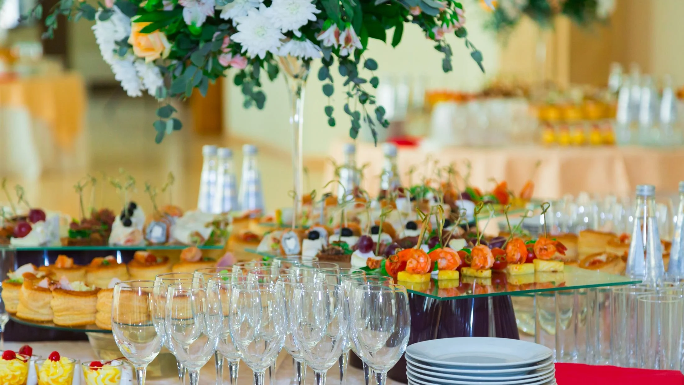 Elegant buffet table with a floral centerpiece and an assortment of appetizers, pastries, and drinks at a celebration or event.