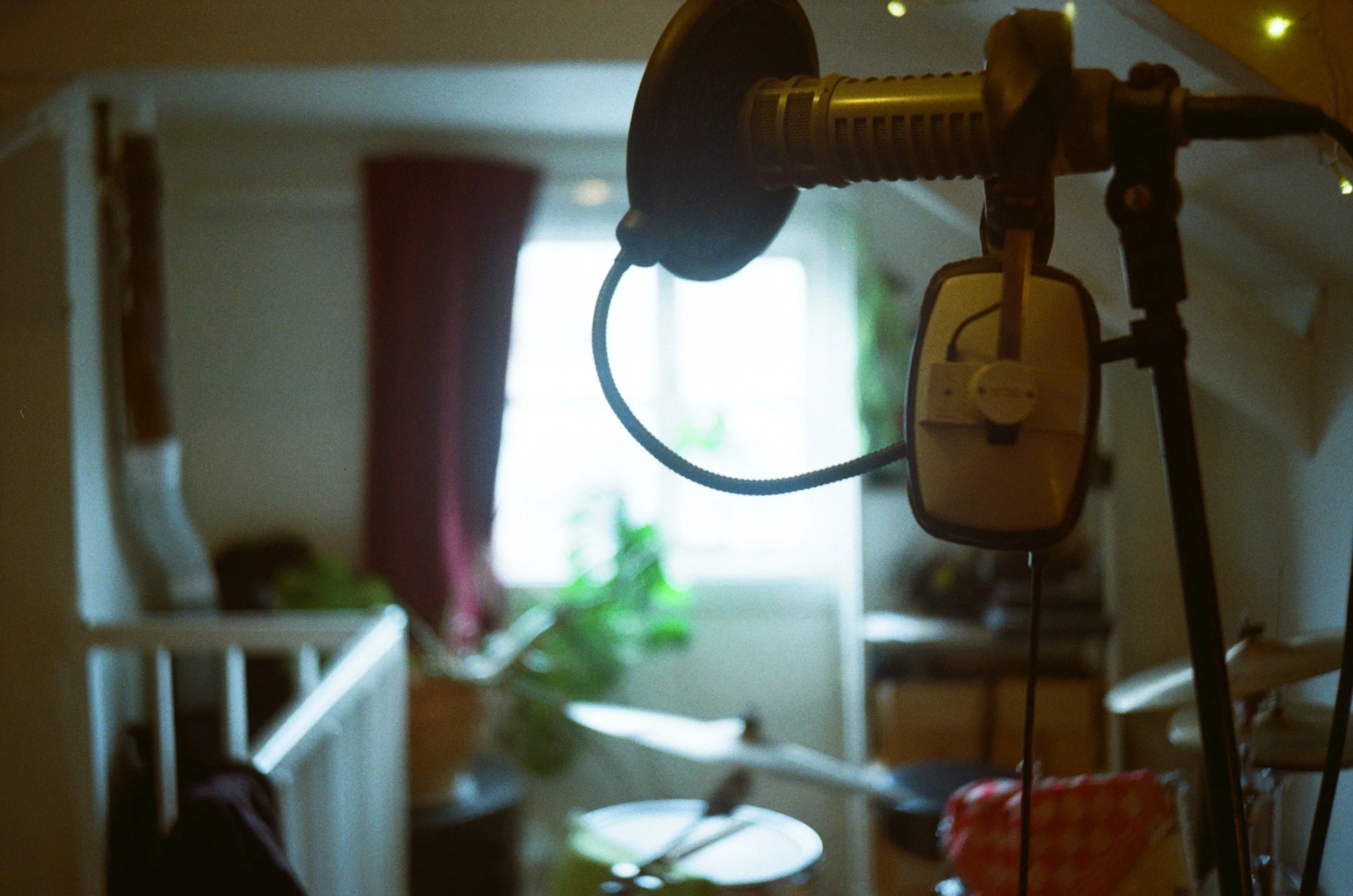 Close-up of a vintage microphone hanging from a stand in a dimly lit room with a window in the background.