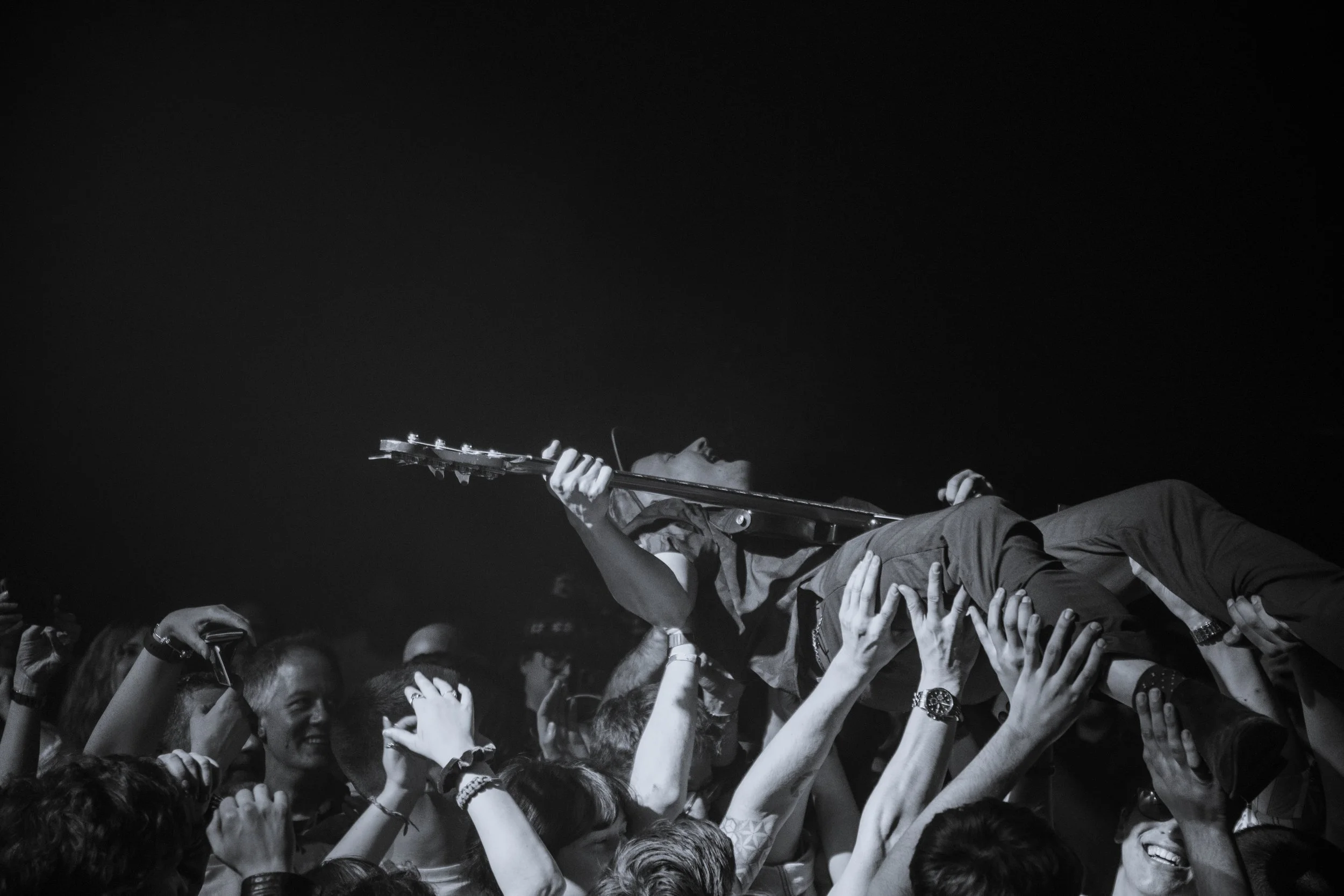 A musician lying on a crowd while playing guitar during a concert, with audience members reaching out towards the performer.