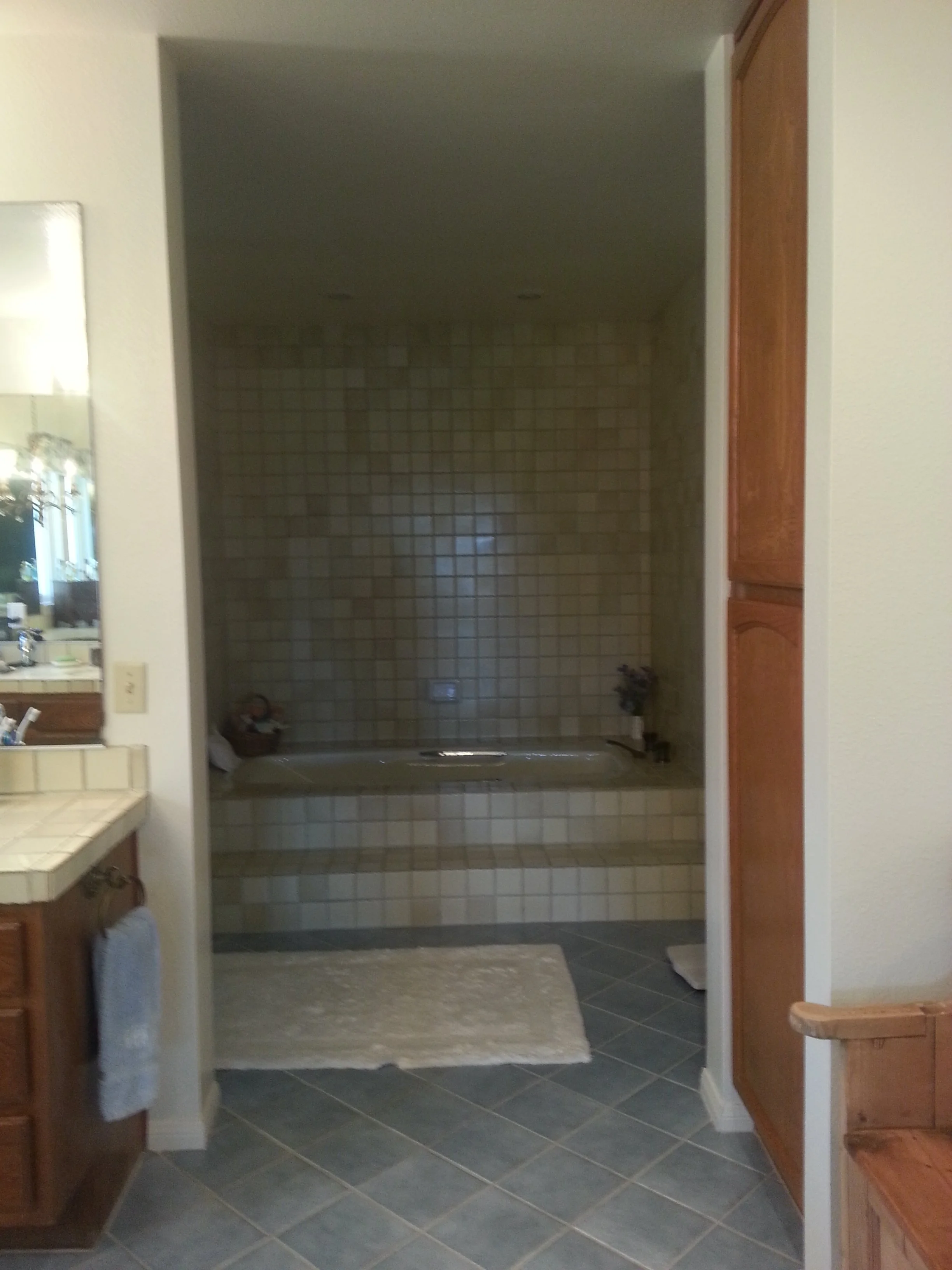 A kitchen with a view into a tiled walk-in shower area, partially obscured by a wall, with a tub visible in the background.