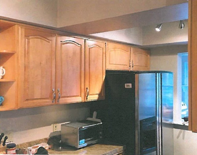 Kitchen with wooden cabinets, black refrigerator, toaster, and a window.