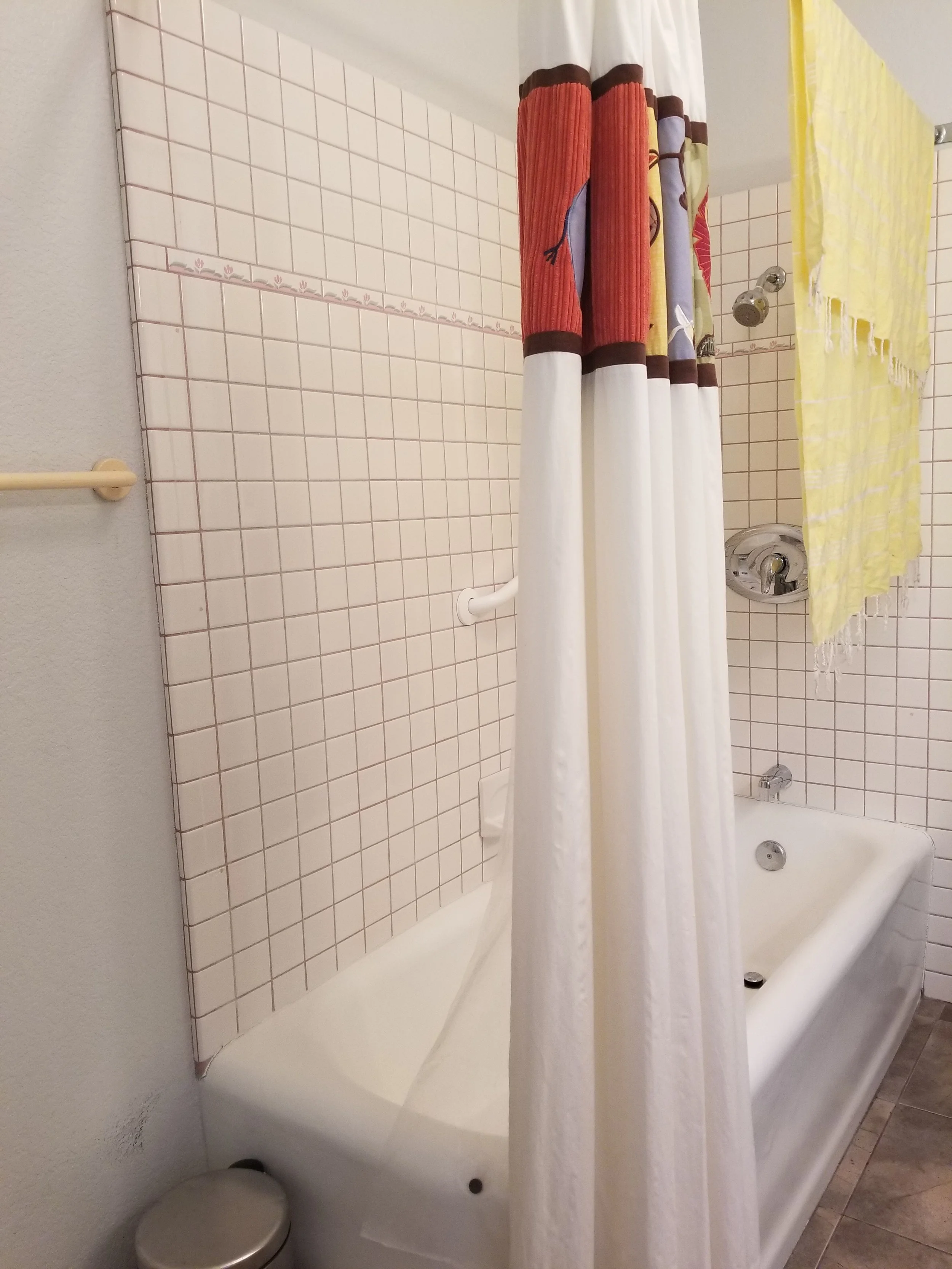 Bathroom with a bathtub, beige tiles on the wall, a shower curtain, and a yellow towel hanging on a wall