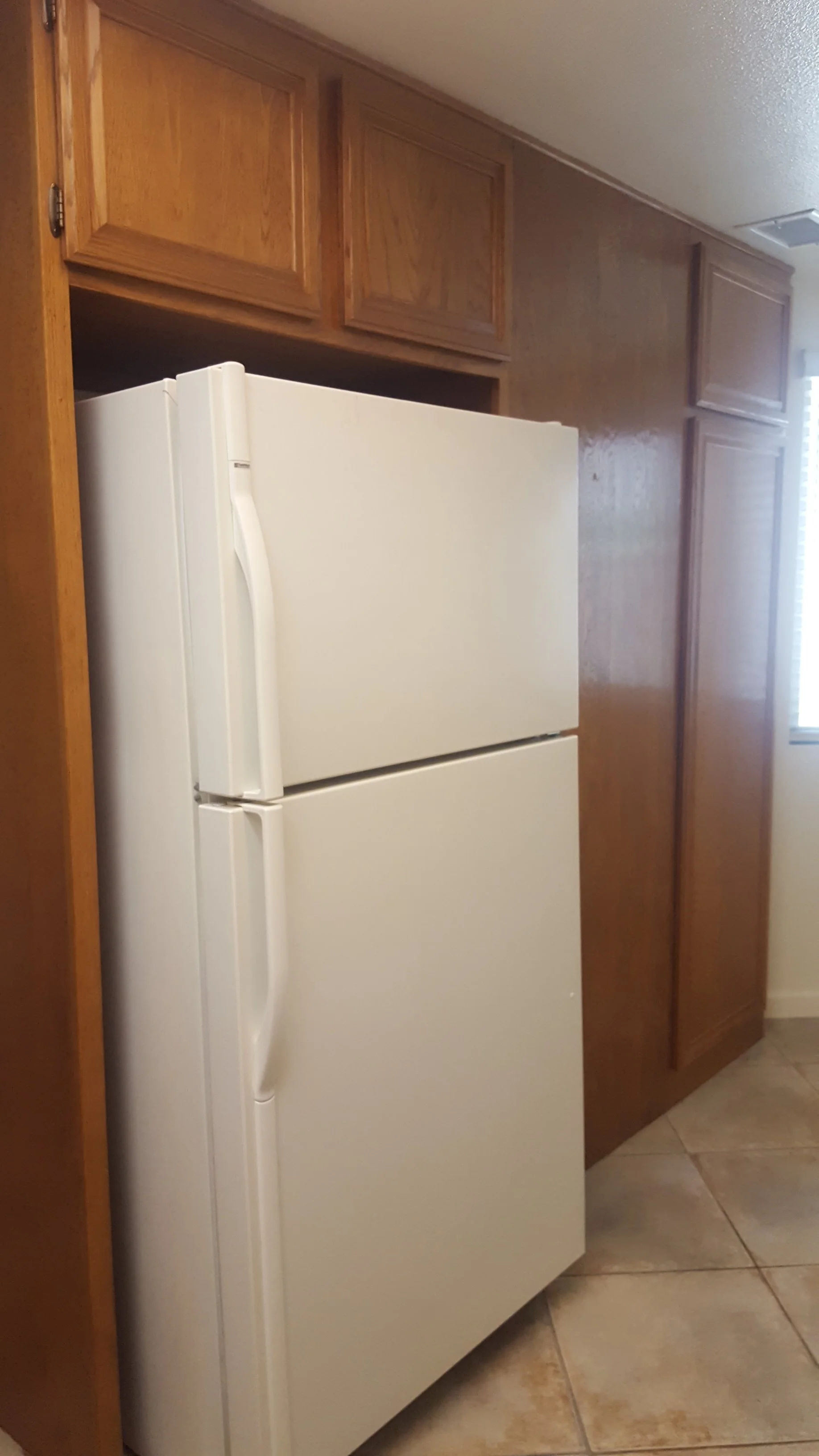 A white refrigerator next to wooden cabinets in a kitchen with tiled floor.