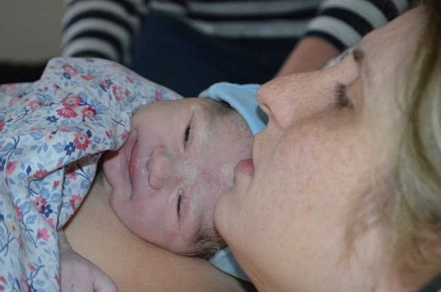 Close-up of a woman holding a newborn baby wrapped in a floral blanket.