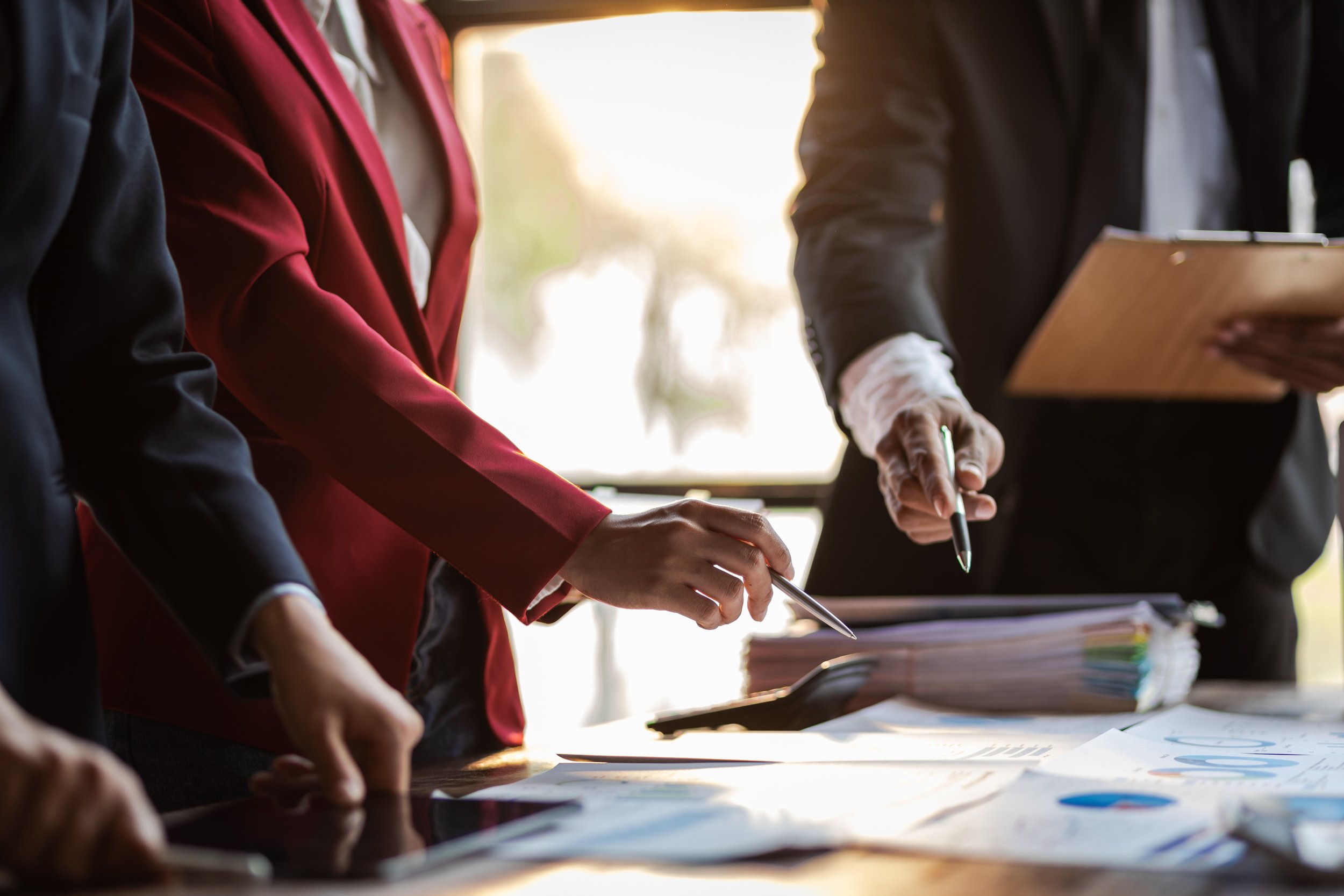 People in business attire signing documents at a desk during a meeting.