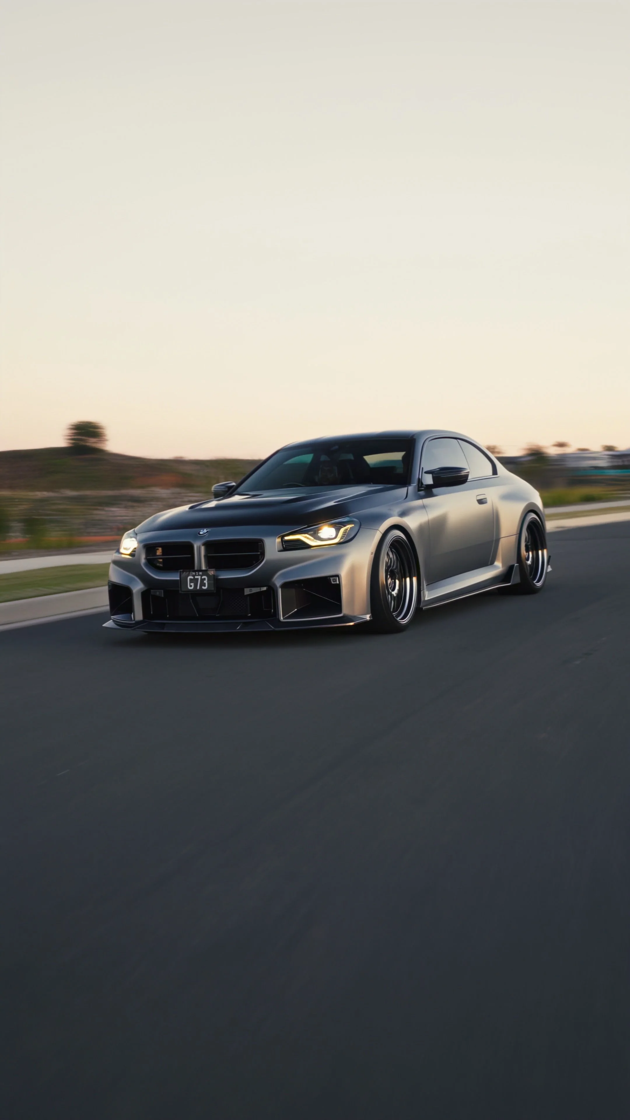 A sleek, dark-colored sports car driving on a highway during sunset.
