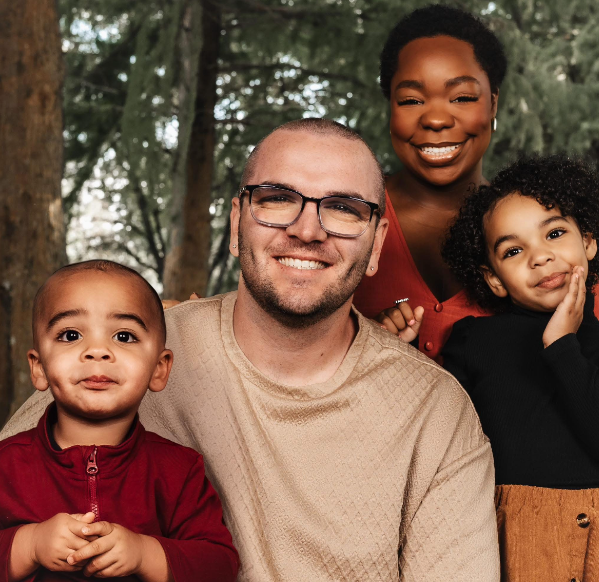 Family portrait of four people outdoors in a park with trees, smiling.