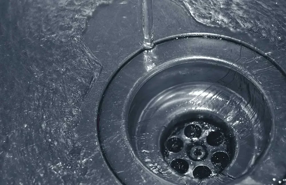 Close-up of a stainless steel sink drain with water flowing into it.