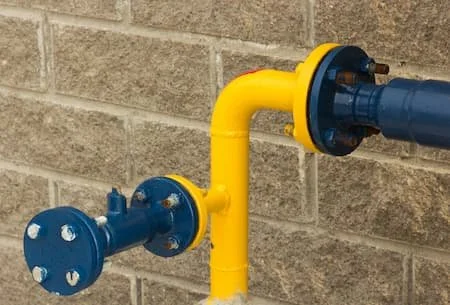 Close-up of blue and yellow gas or water pipes attached to a brick wall.