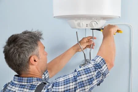 A plumber working on a water heater using a screwdriver