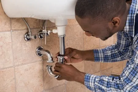 A man fixing or inspecting the plumbing under a kitchen sink.