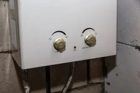 A white wall-mounted water heater with two control knobs and a small red indicator light.