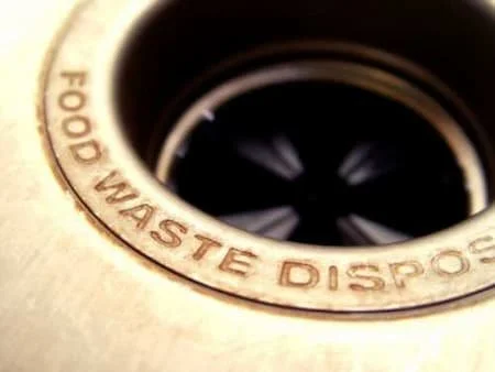 Close-up of a garbage disposal unit in a kitchen sink with the label 'FOOD WASTE DISPOSAL' around the drain opening.