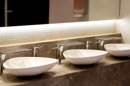 Three white oval sinks with silver faucets on a beige marble countertop in a bathroom.