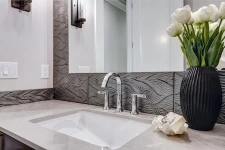 Bathroom with a sink, a large mirror, a black vase with white tulips, and textured wall paneling.