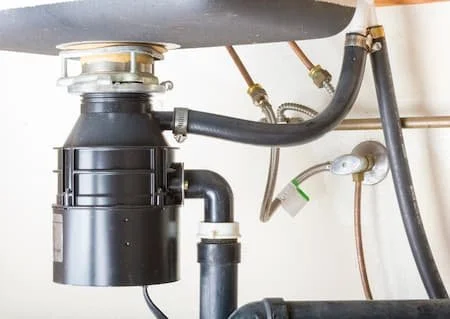 Underneath a kitchen sink showing plumbing pipes and a garbage disposal unit.