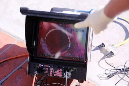 Close-up of a thermal imaging camera screen showing a thermal image of a person's hand wearing a glove, with cables and equipment around on a flat surface.