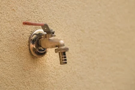 An outdoor water faucet attached to a beige wall.