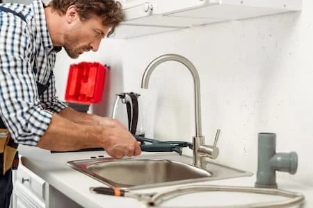 A man working on a kitchen sink with tools.