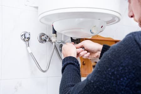 Person repairing or installing a water heater in a utility room.