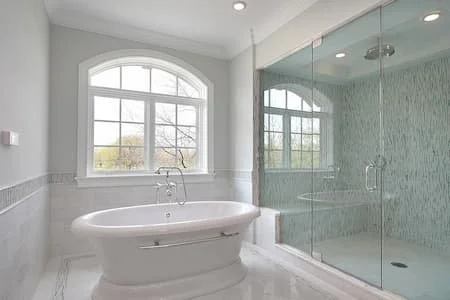 Bathroom with a large arched window, bathtub, and glass-enclosed shower.