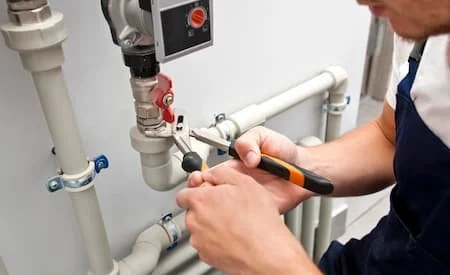 A person working on plumbing pipes near a water meter or valve
