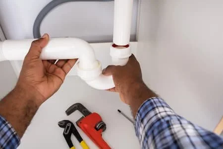 Person working with white plumbing pipes and tools on a white surface
