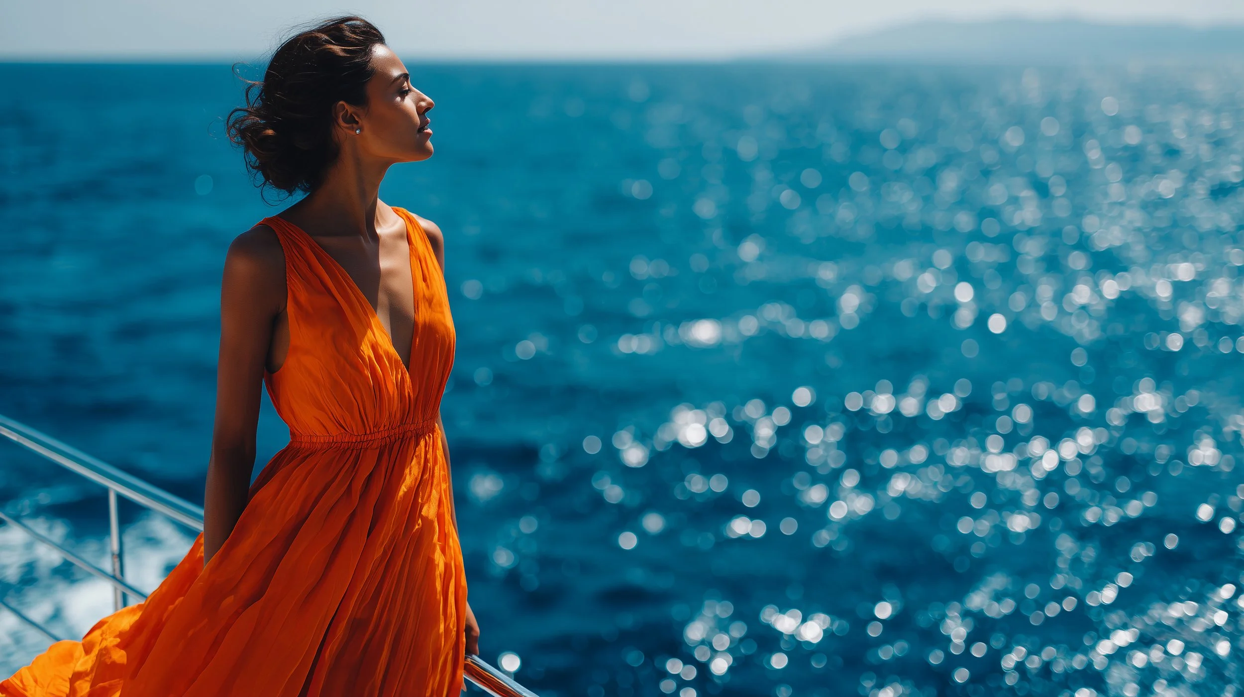 A woman in an orange dress standing on a boat, with the ocean in the background and sunlight reflecting on the water.