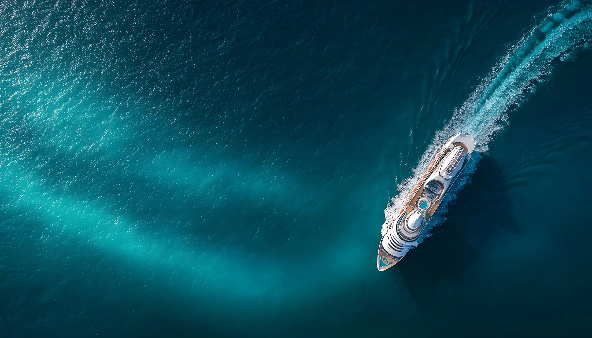 A yacht sailing in the ocean, creating a wake behind it, with clear blue waters.
