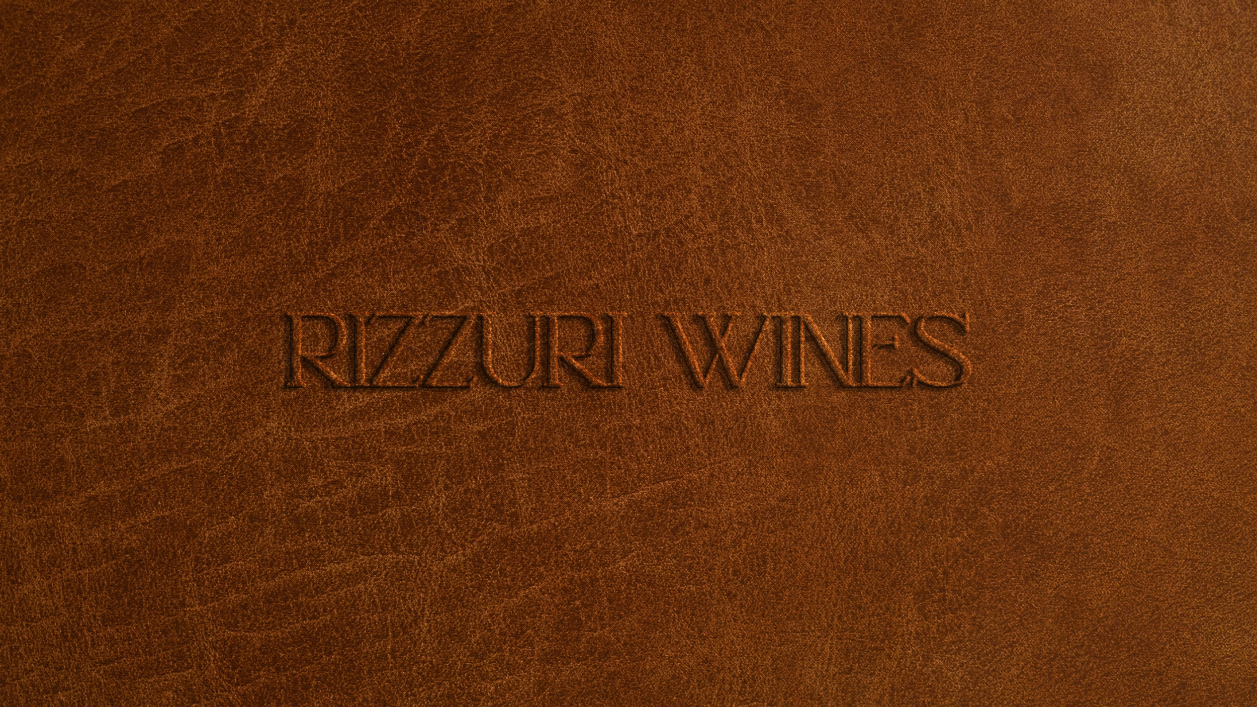 Texto en relieve que dice 'RIZZURI XINES' en un fondo de cuero marrón.