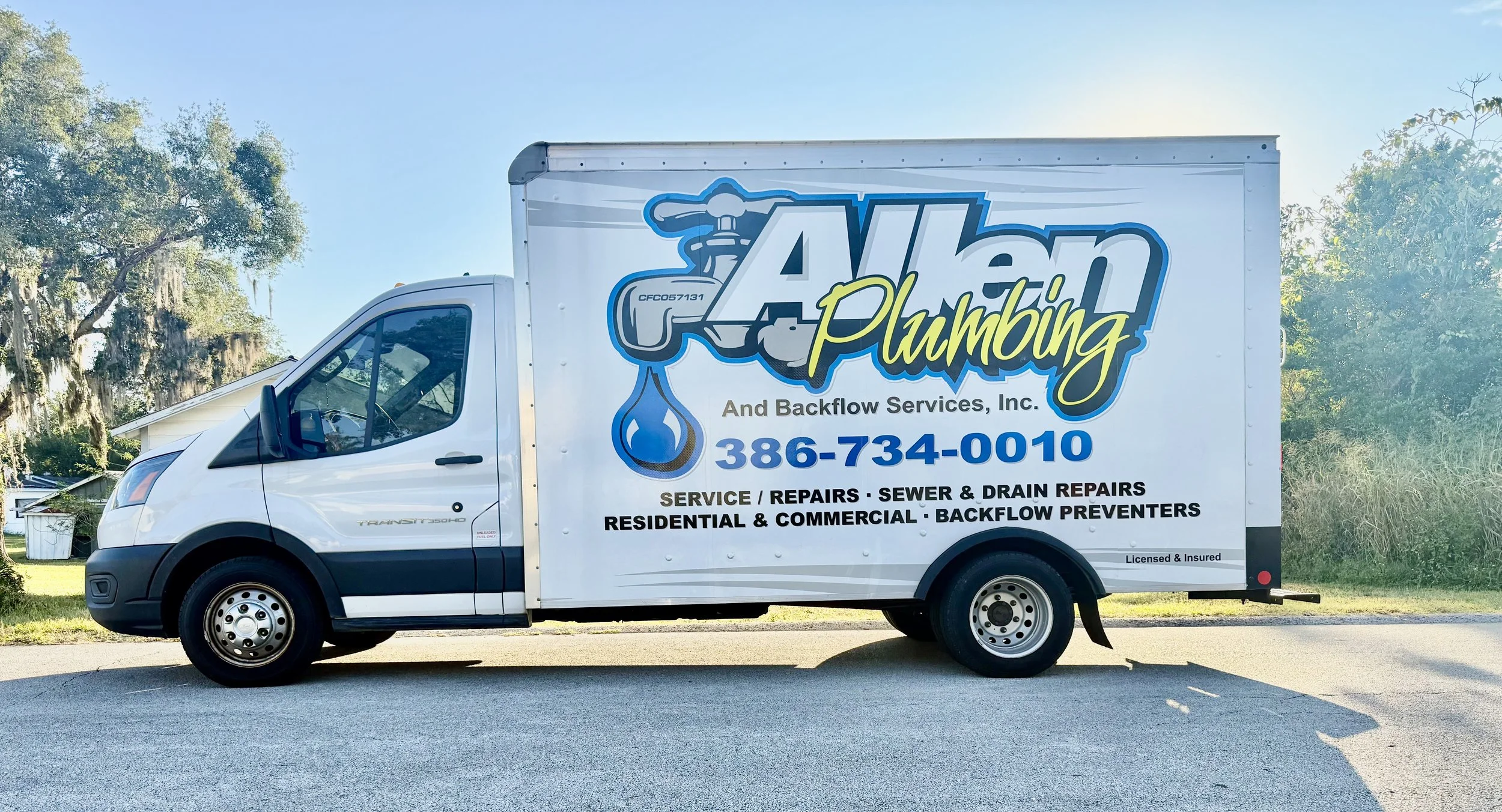 White service van with the logo and contact information for Allen Plumbing and Backflow Services Inc., parked on a neighborhood street with trees and a house in the background.