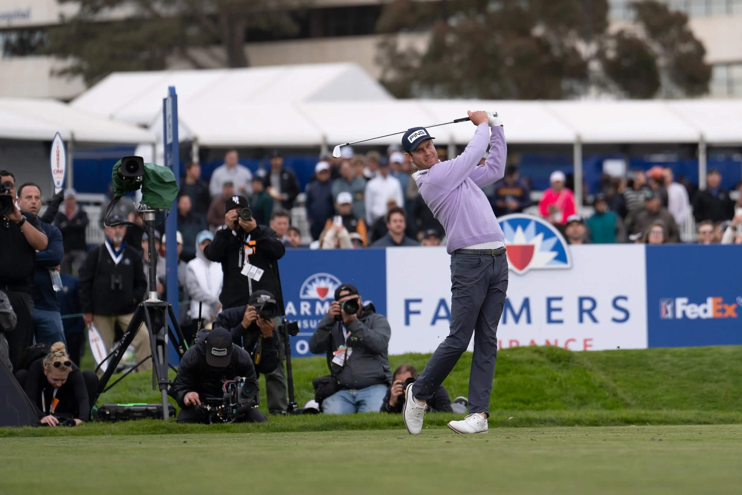 A golfer swinging a club on a golf course with a crowd of spectators and photographers in the background