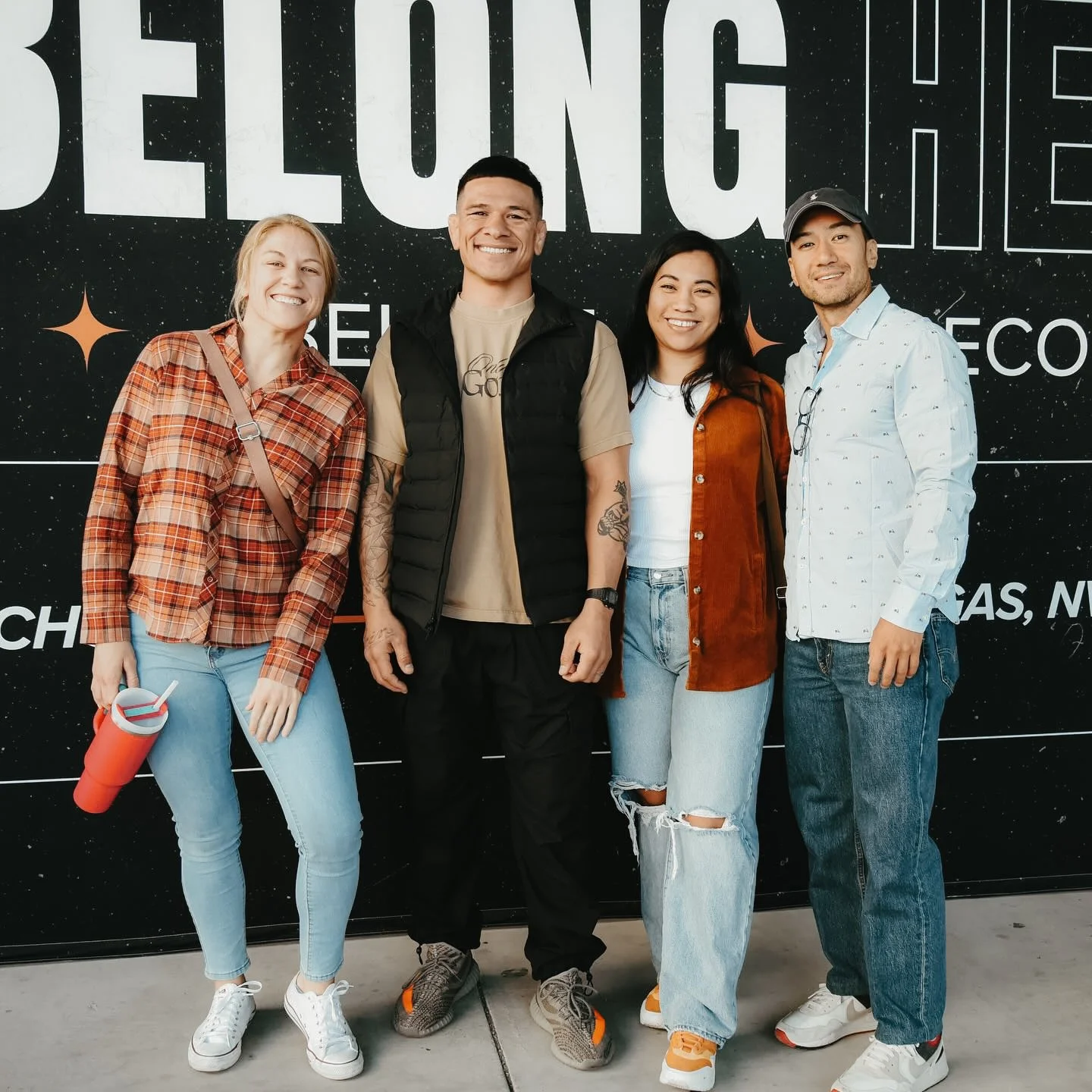 Four people smiling and standing together in front of a black background with large white text and stars.