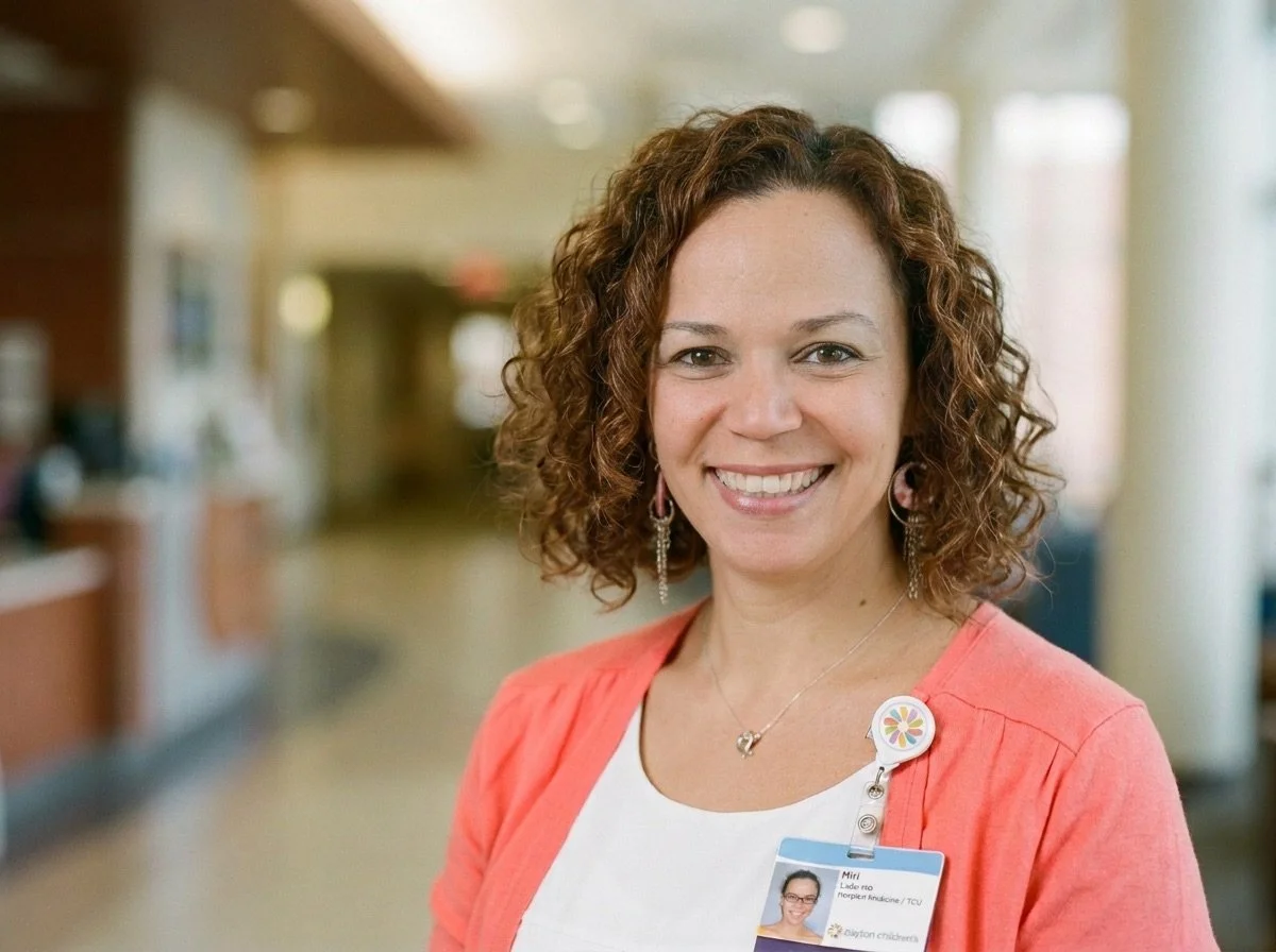 Dr. Lader Smiling in a hospital or medical facility, wearing a name badge and a coral blazer.