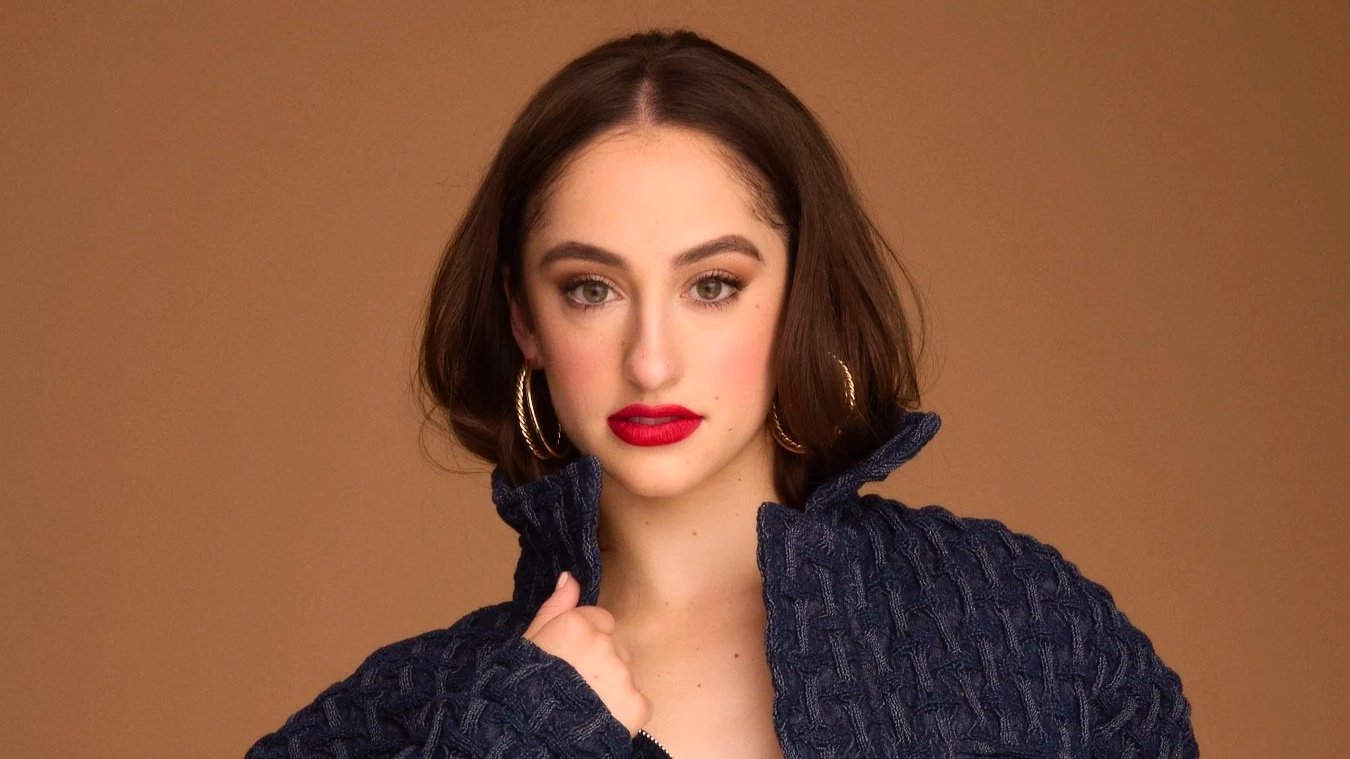 A woman with shoulder-length brown hair, wearing hoop earrings and a navy textured jacket.
