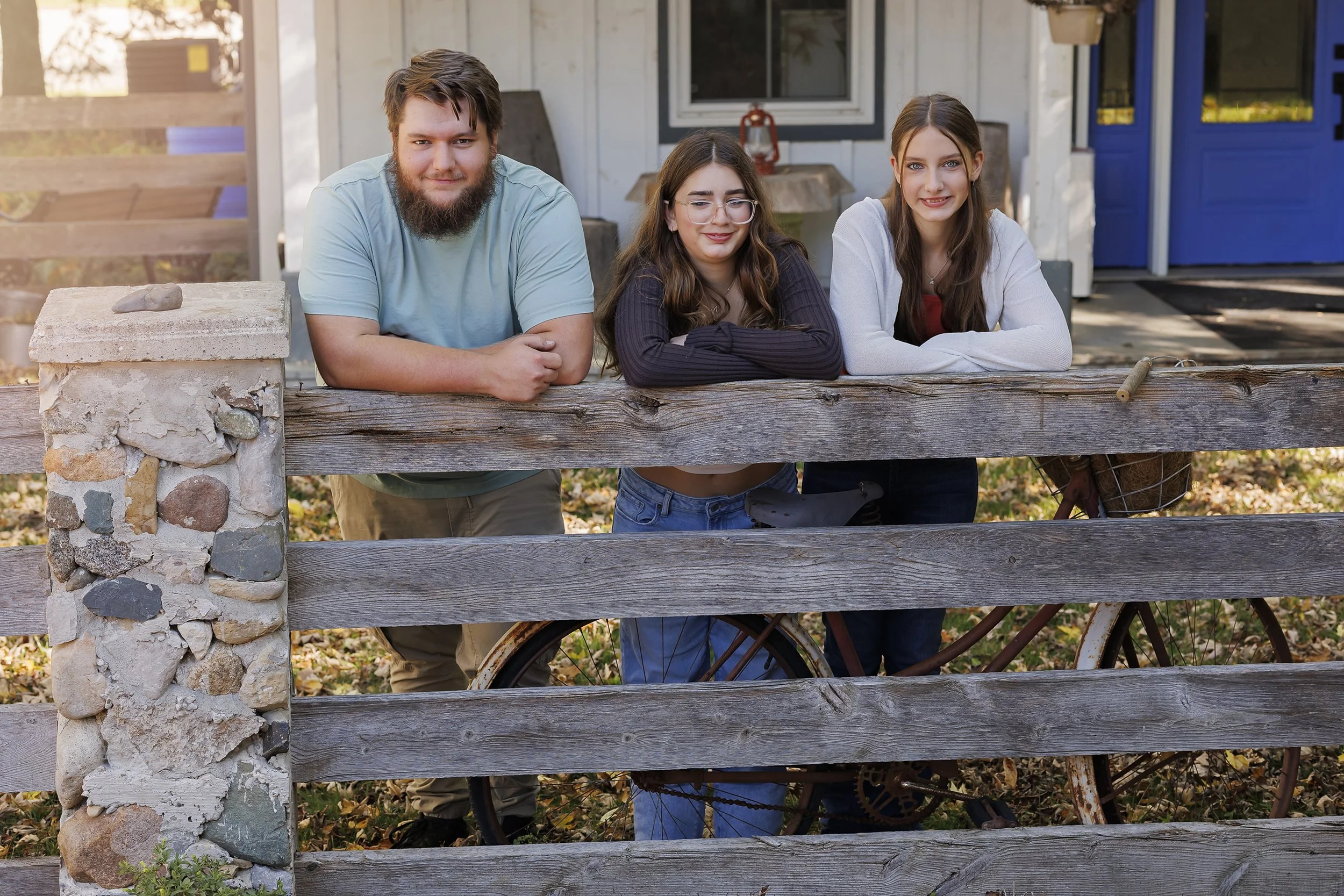 Family portrait in Waterloo Region and St. Jacobs by Janelle Joy Studios — Three people leaning on a rustic wooden fence in a cozy outdoor setting.