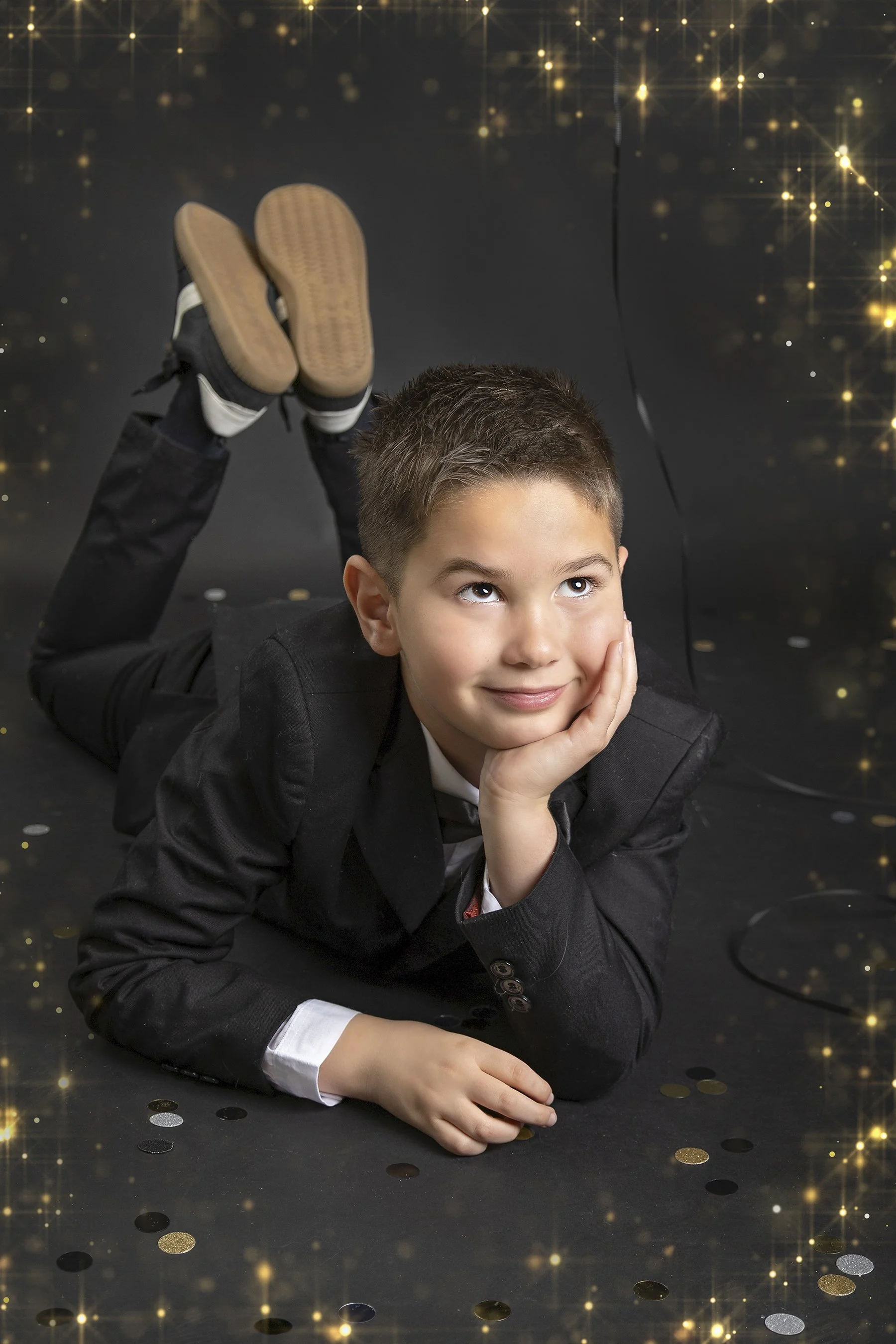 Studio portrait with celebratory confetti by Janelle Joy Studios — Youth lying in a playful pose surrounded by gold and silver confetti.