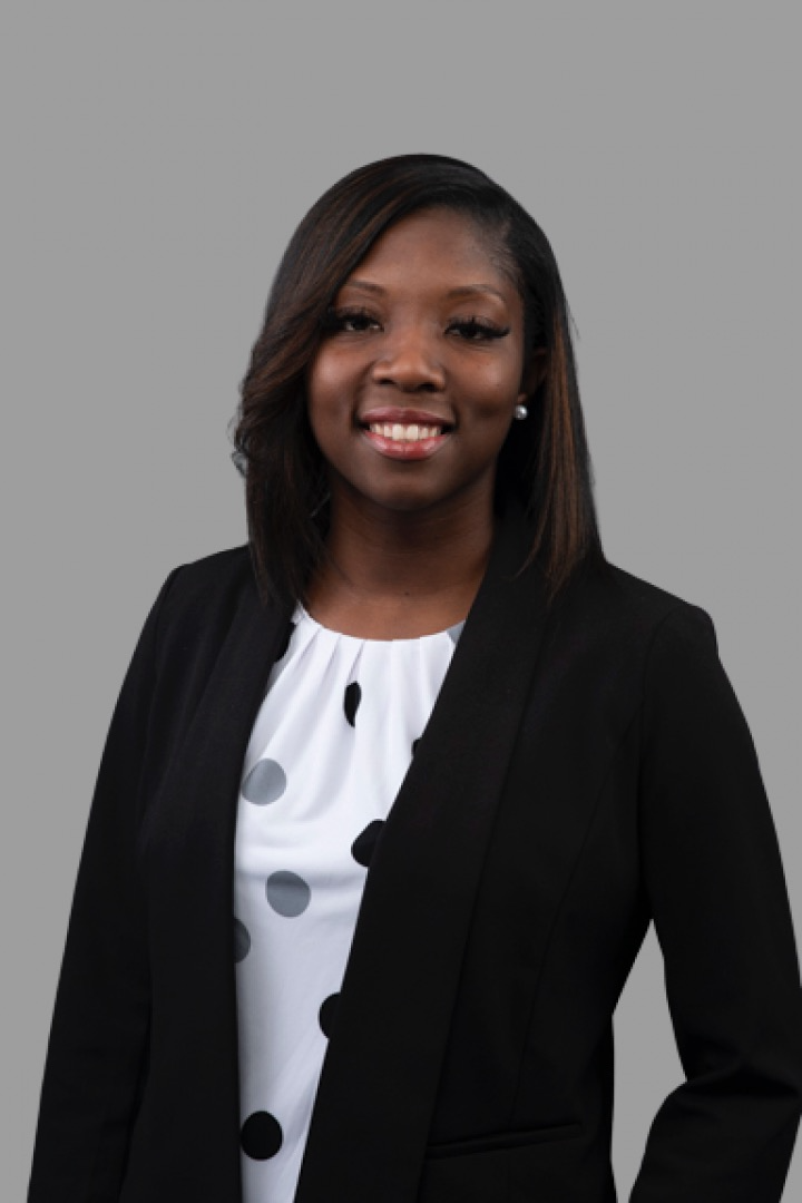 Headshot of licensed therapist, Brittany Davis, a smiling Black woman with shoulder-length hair, wearing a black blazer and a white blouse with black and gray polka dots, against a plain gray background.