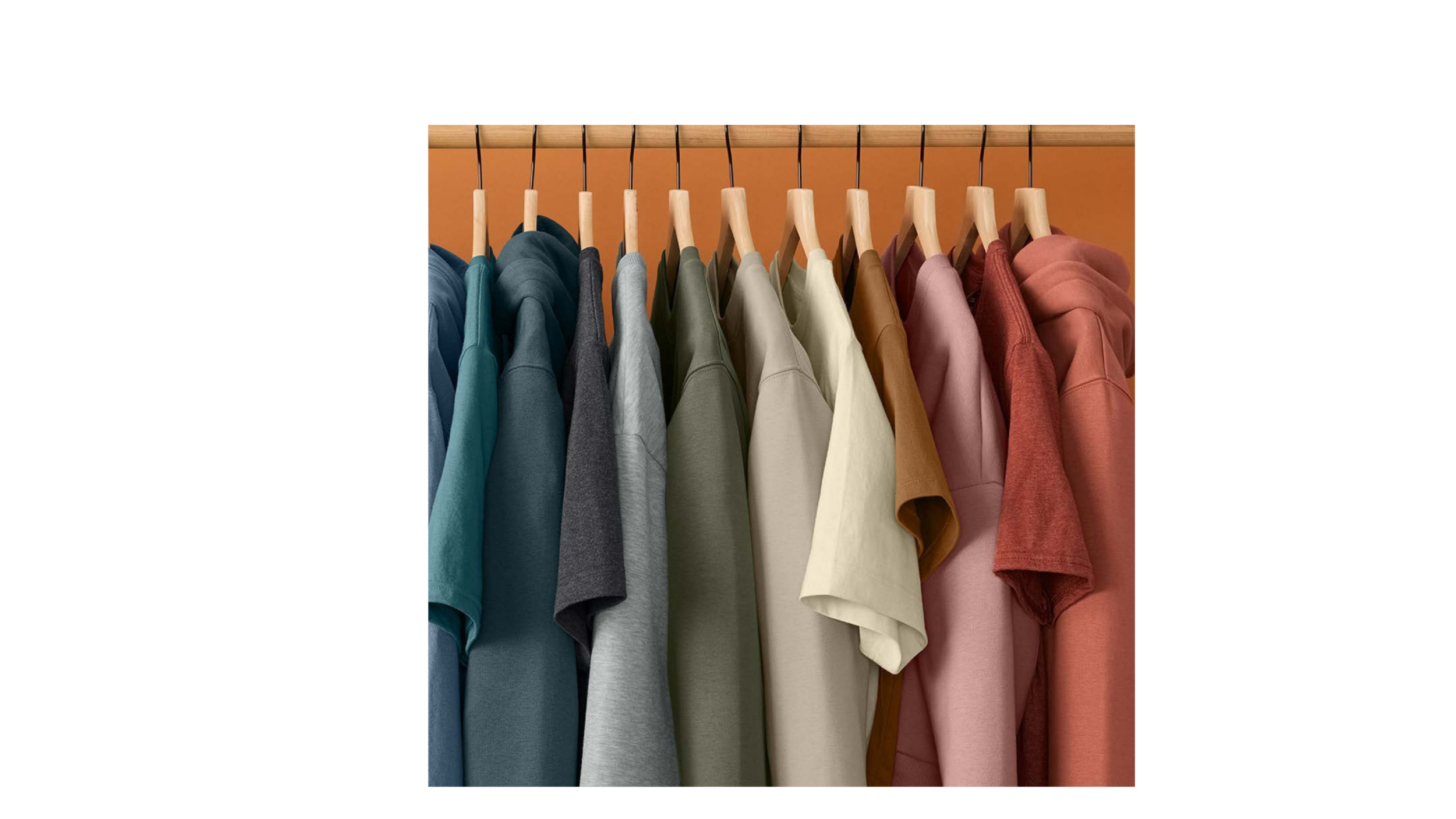 A row of colorful T-shirts hanging on wooden hangers on a clothing rack, arranged from blue to pink.
