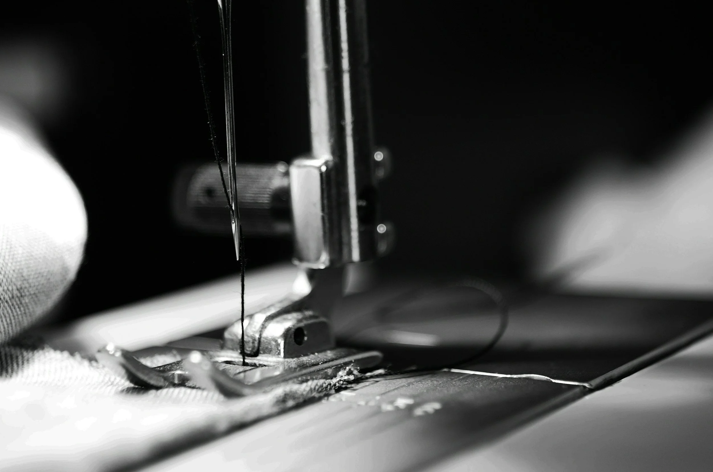 Close-up of a sewing machine needle and presser foot, with black and white focus on metal parts.
