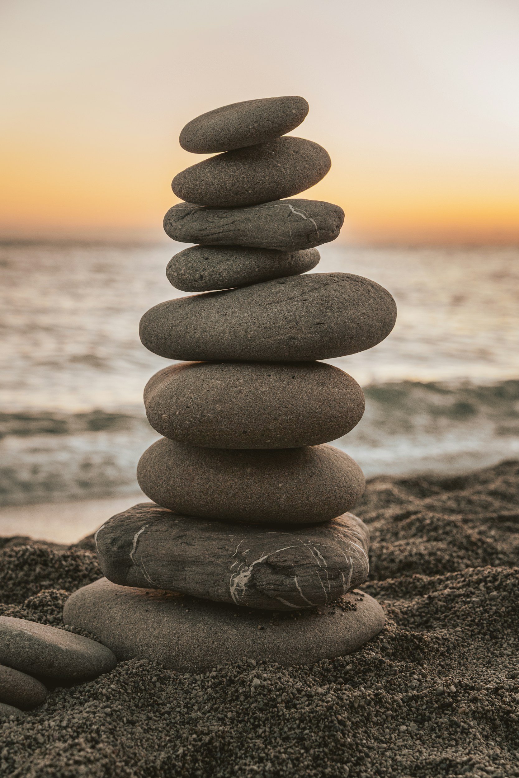 Stacked smooth stones on a sandy beach at sunset.