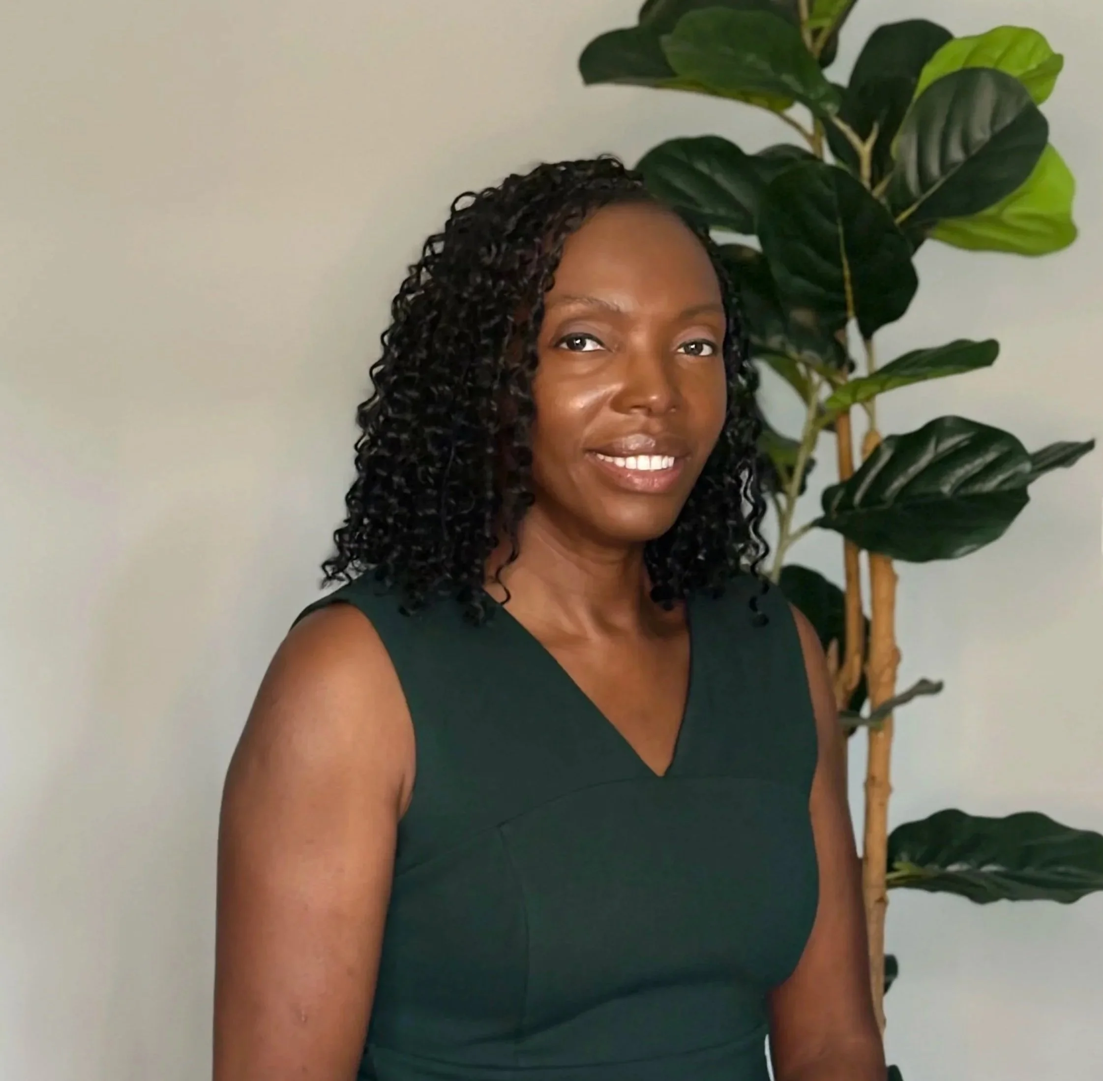Bertha Biag, founder of Broadview Collective, smiling in a dark green top beside a leafy plant.