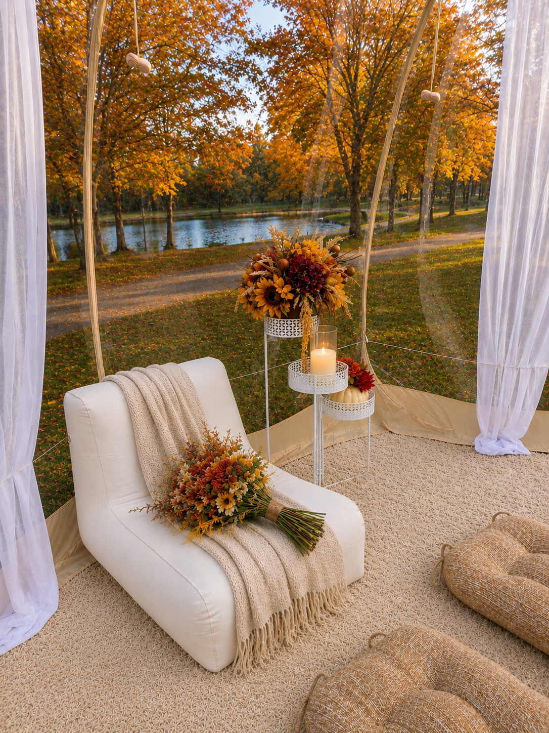 Luxury fall picnic in a clear pop-up tent in Minnesota featuring elegant lounge seating, cozy blankets, seasonal floral décor, candles, and a peaceful outdoor setting overlooking colorful autumn trees and a pond.