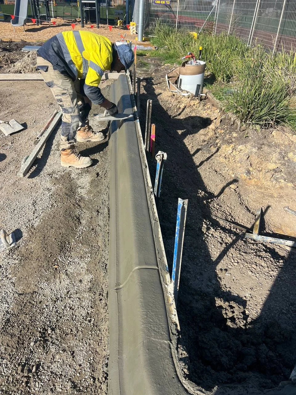 Construction worker smoothing wet concrete along a pathway at a construction site.