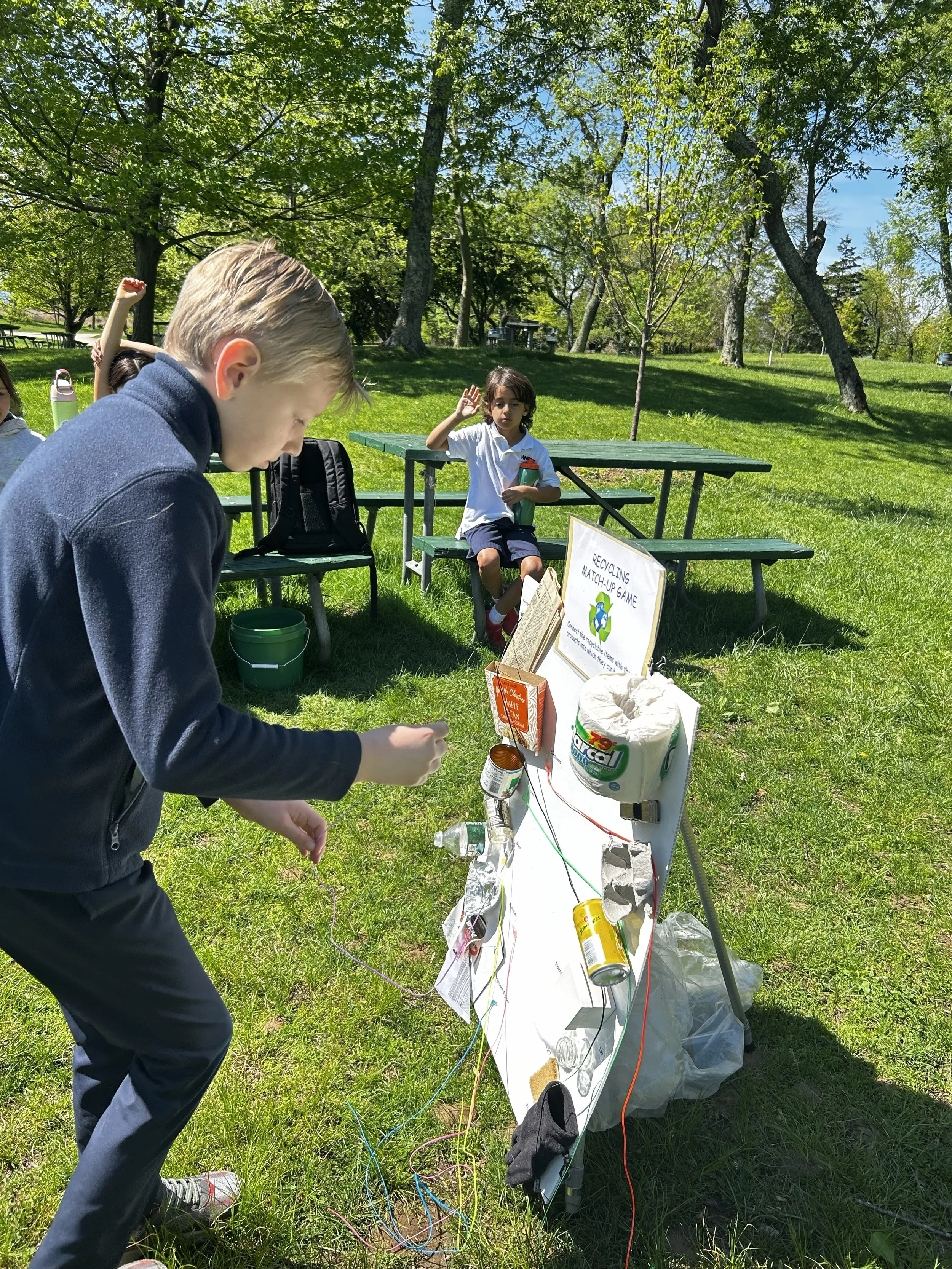 A second grader explores where everyday materials come from through a hands-on recycling match-up game, following a beach cleanup as part of a Reduce, Reuse, Recycle unit.